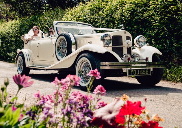 Bride wearing sunglasses riding in an ivory convertible vintage wedding car.