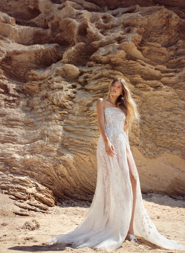 Model is on the beach and wearing a thigh-high split in the voluminous silver and sequinned embroidered tulle dress