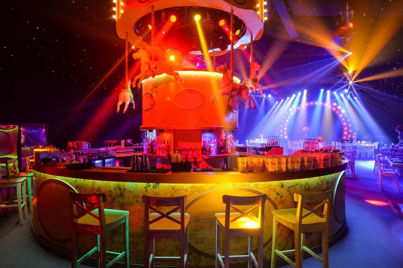 indoor event at night lit by coloured lights with a focal point central bar