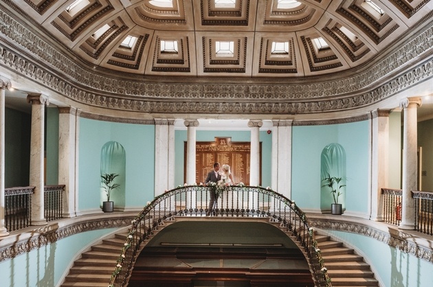 Bride and groom stood at top of grand staircase at Leigh Court wedding venue in Bristol.