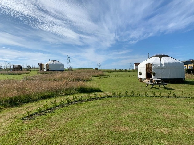 yurt in manicured grounds surround by flat grass and a couple of other yurts