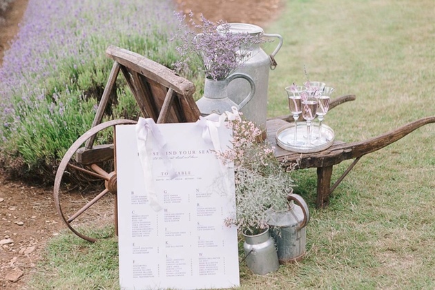 Rustic wheelbarrow and milk urn dressed with wedding flowers and table plan.