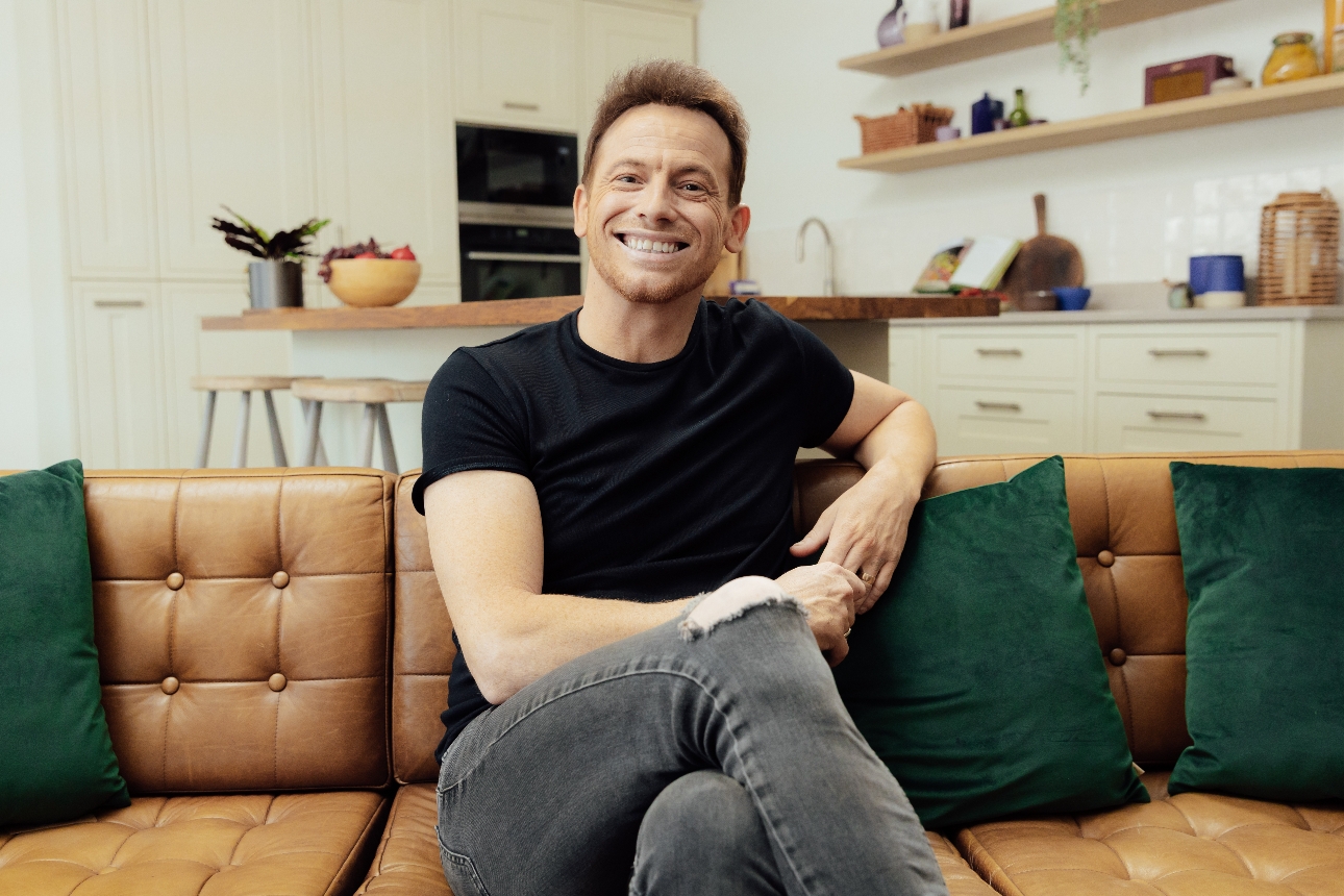 Joe Swash on a brown leather sofa in a kitchen