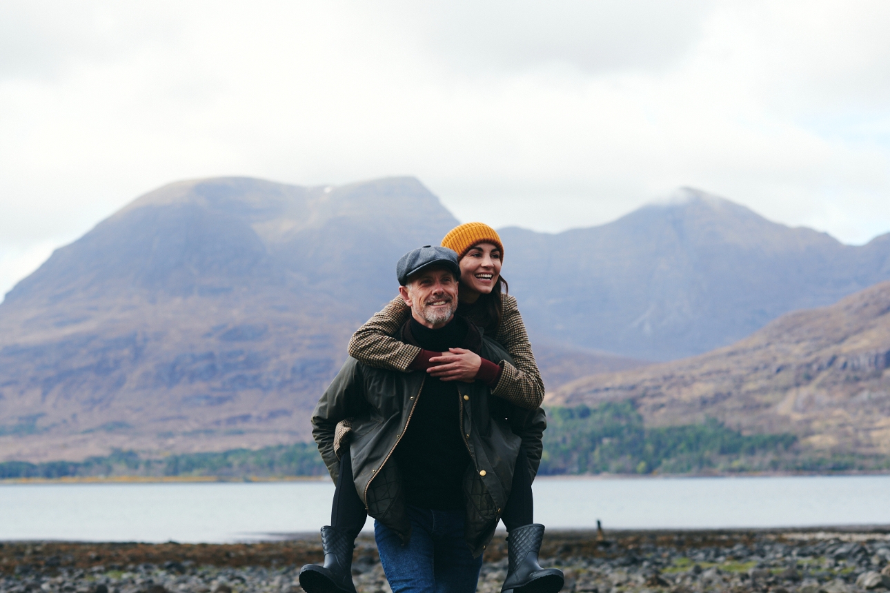 woman having a piggy back on a man with the highlands in the background and lake