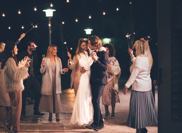 bride and groom dancing outside with guests waving sparklers 
