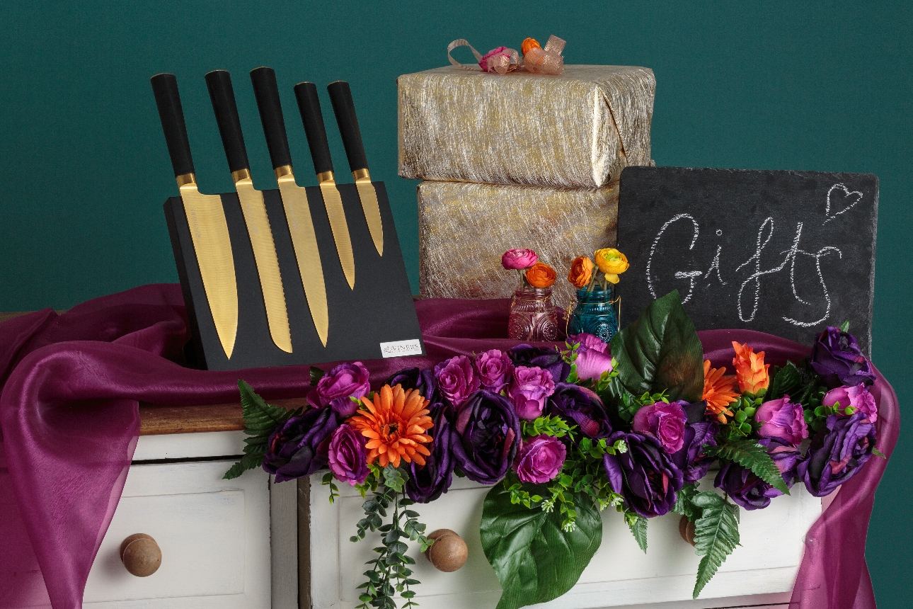 knife block with gold knives on a chest of drawers with a bunch of flowers and a sign saying gifts