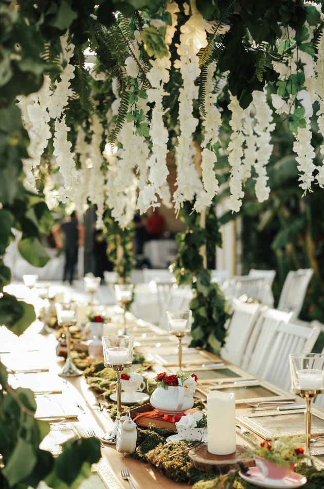 wedding reception table set up with plates and napkins with large floral displaying hanging down above