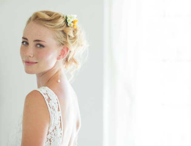 blonde bride with blue eyes with her hair up and a white dress with lace shoulders on