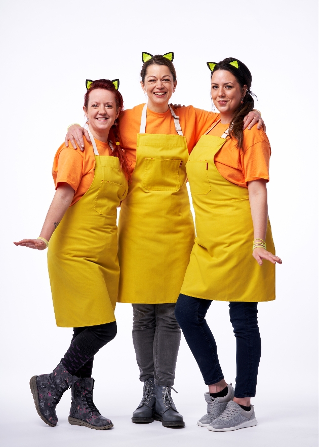 Three women wearing yellow aprons posing for the camera