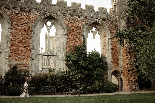 Bride and groom walking through the gardens at the Bishops Palace with view of Wells Cathedral in the background