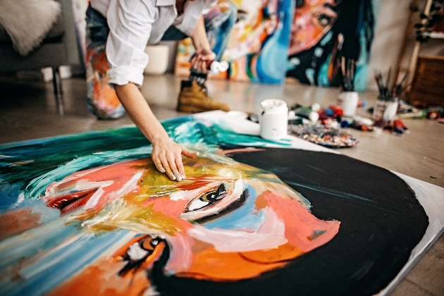 Person crouching on the floor creating a painting of a woman using finger painting. 