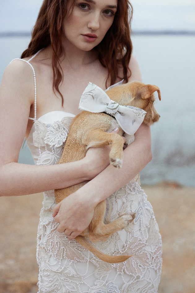 model in lace dress with thin straps holding a dog with a bow on 