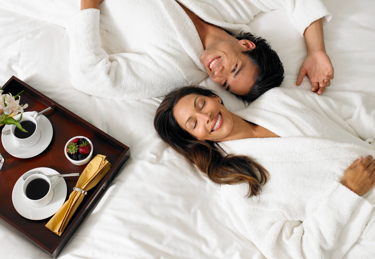 couple in robes laying on bed with breakfast 