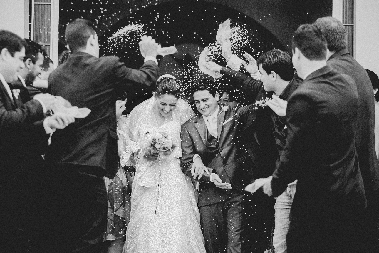 black and white image of a bride and groom leaving church and guests throwing confetti on them